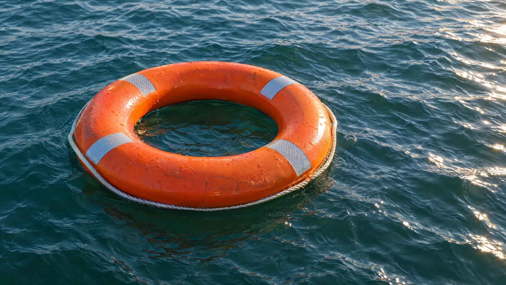 Geschlossener orangefarbener Rettungsring auf leicht bewegtem blaugrünem Wasser.