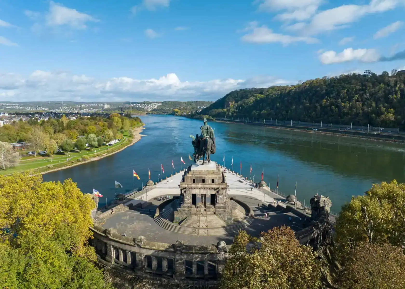 Deutsches Eck in Koblenz von oben: das Reiterdenkmal auf der Landspitze zwischen Mosel und Rhein, dahinter der Rhein und bewaldete Hänge
