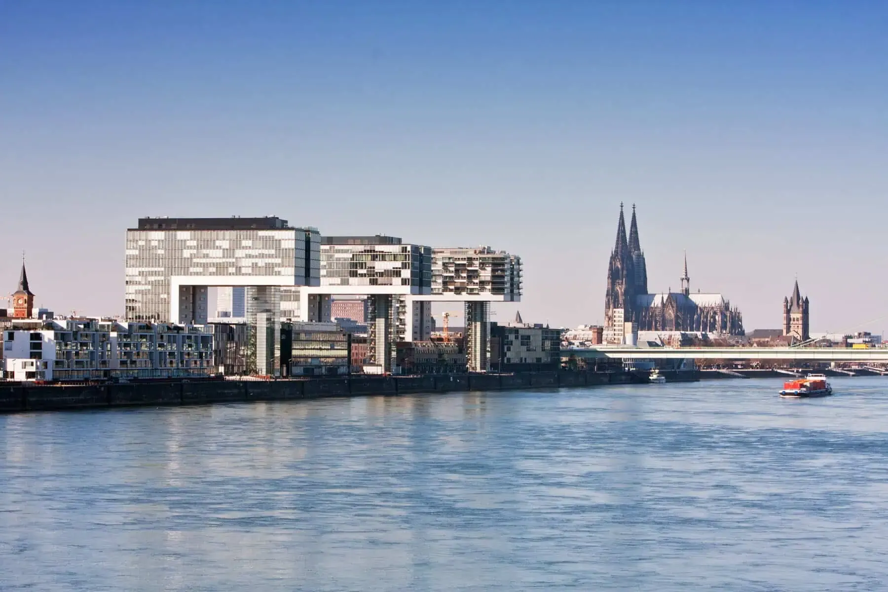 Rheinpanorama in Köln: die Kranhäuser am Rheinauhafen, dahinter der Kölner Dom, auf dem Rhein ein Frachtschiff