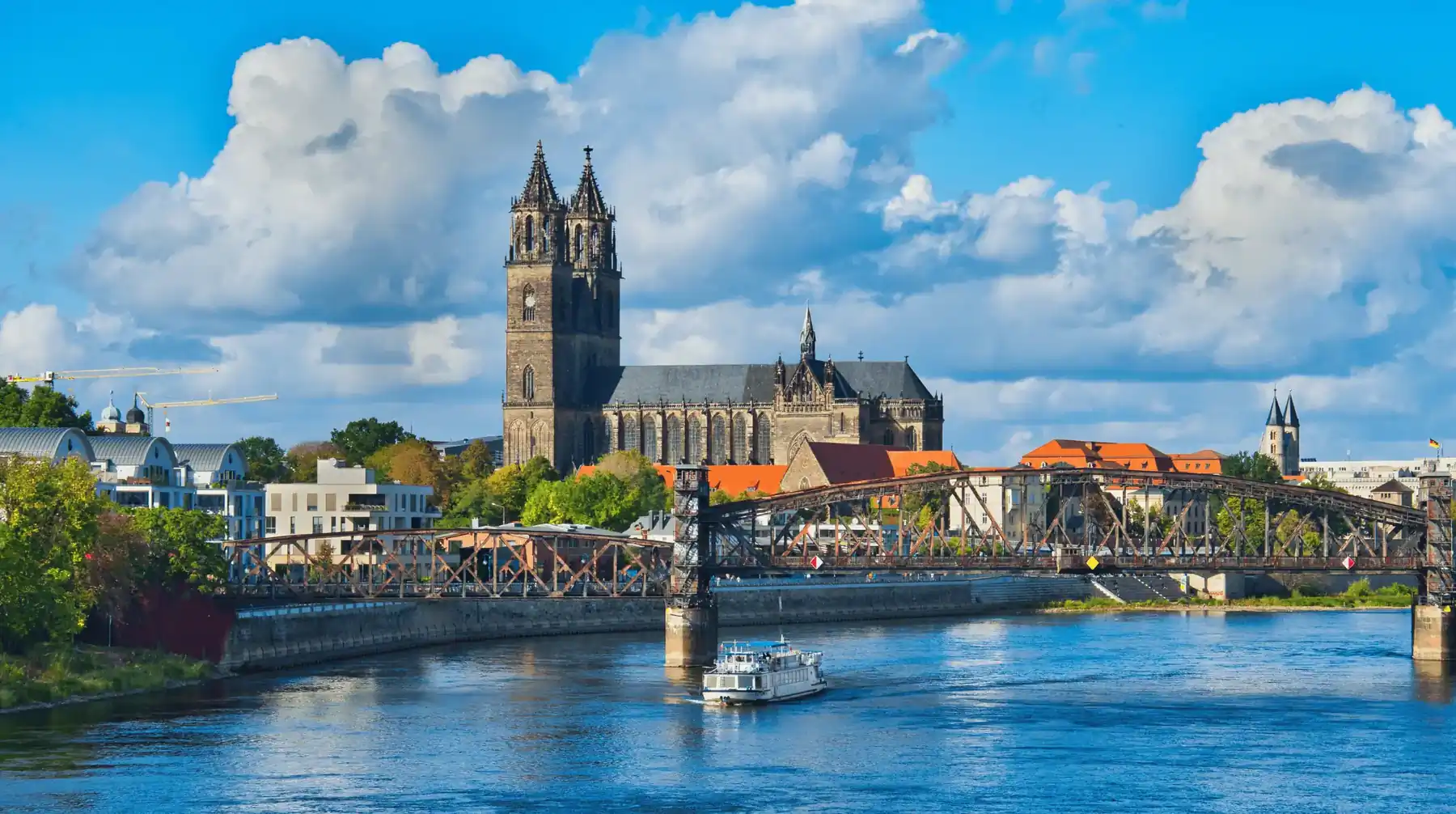 Die Elbe in Magdeburg bei Sonne: ein Fahrgastschiff fährt auf die stählerne Hubbrücke zu, dahinter der Magdeburger Dom über dem Ufer